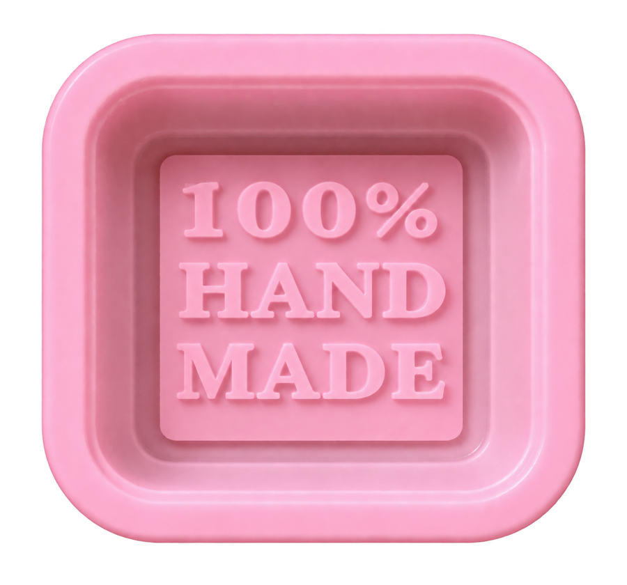 A pink square soap bar with rounded corners, featuring the embossed text '100% HAND MADE' in the center, isolated on a white background.